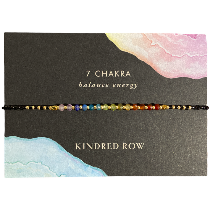 The Chakra Healing Gemstone Stacking Bracelet by Kindred Row is a handcrafted piece adorned with multicolored beads crafted from natural gemstones representing the 7 chakras. It is elegantly presented on a card inscribed with "7 CHAKRA balance energy" and "Kindred Row," featuring delicate watercolor designs, and includes an adjustable cord for an ideal fit.