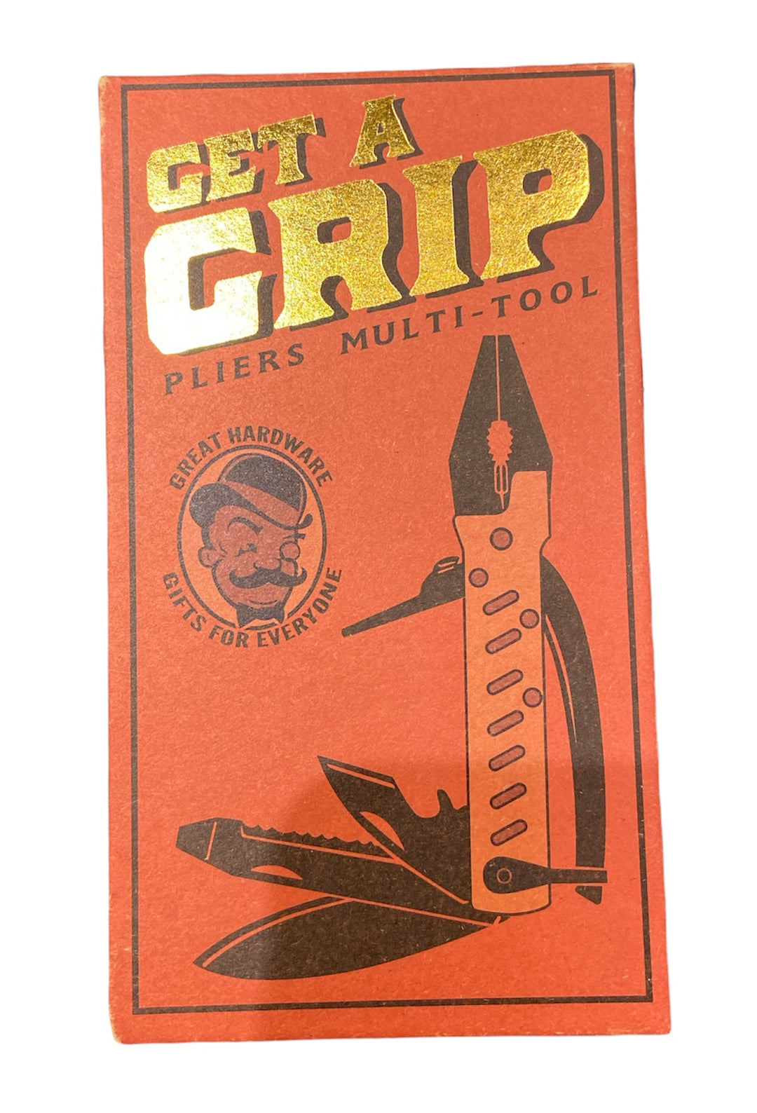 The red packaging for the Get a Grip Multi Pliers by TrixienMilo showcases the text "GET A GRIP" in gold, accompanied by "PLIERS MULTI-TOOL" and "GREAT HARDWARE GIFTS FOR EVERYONE," artistically arranged around an illustration of a man's face. This image emphasizes the multi-tool's versatility, featuring pliers and wire cutters.