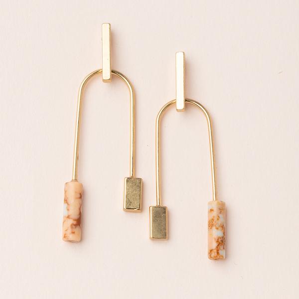 Introducing the Stone Balance Earring Pink Gold by Scout Jewelry, a pair of exquisite gold dangle earrings featuring rectangular and cylindrical shapes with marbled beige and white accents, complemented by dipped brass highlights, all presented on a neutral background.