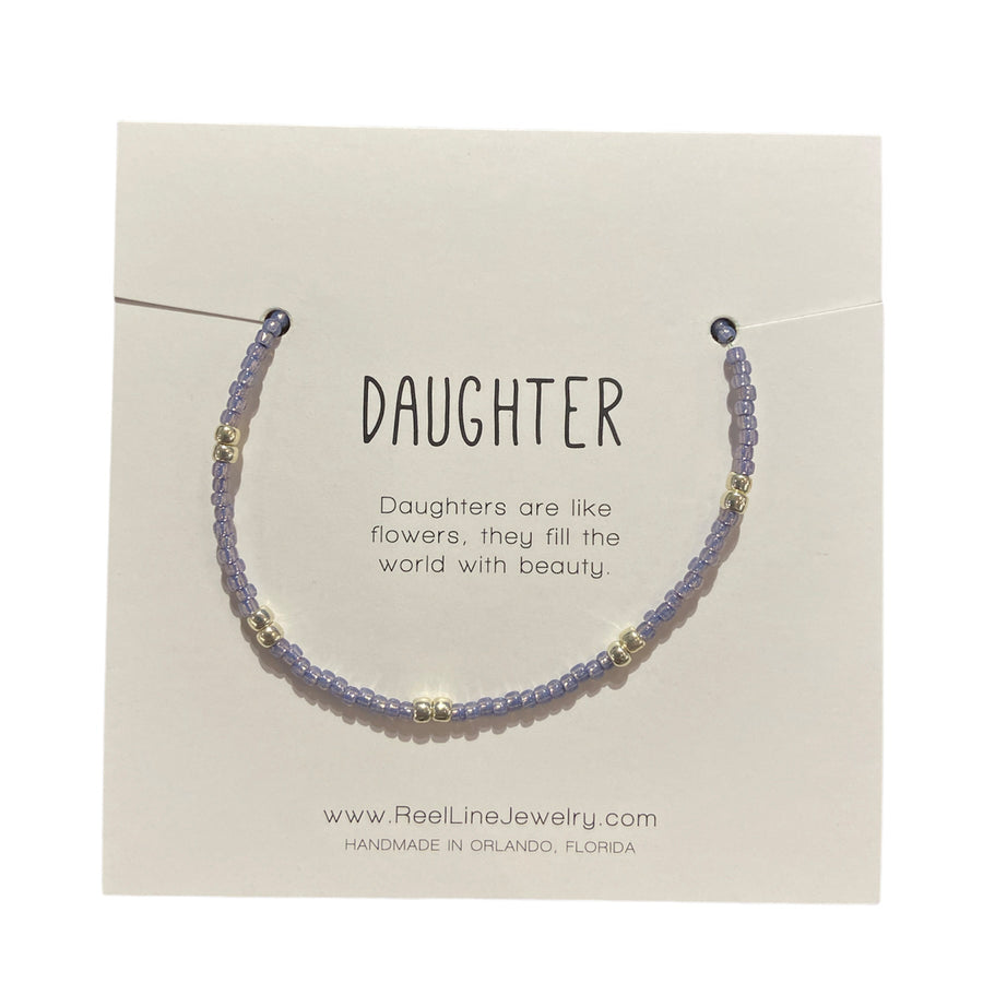 The Daughter - Violet and Silver, a thin glass beaded bracelet with light purple and silver beads, is displayed on a card inscribed with, "Daughter. Daughters are like flowers, they fill the world with beauty." This handcrafted jewelry by Reel Line Jewelry features adjustable links and is made in Orlando, Florida.