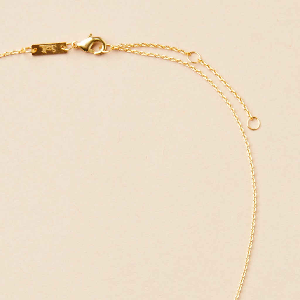 The Refined Neck Comet in 18k gold vermeil, by Scout Jewelry, is gracefully showcased on a light beige surface. This exquisite necklace features a fine chain and small lobster clasp, with two small rings near the clasp for adjustable sizing, enhancing its elegant and refined design.
