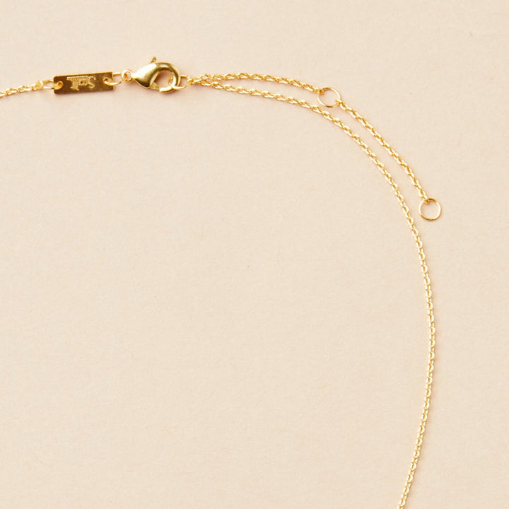 The Refined Neck Comet in 18k gold vermeil, by Scout Jewelry, is gracefully showcased on a light beige surface. This exquisite necklace features a fine chain and small lobster clasp, with two small rings near the clasp for adjustable sizing, enhancing its elegant and refined design.