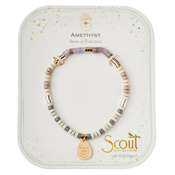 An Intention Charm Amethyst Gold bracelet from Scout Jewelry is displayed on white packaging. The bracelet features alternating small beads in various neutral shades and gold accents, highlighting a 14k gold-dipped charm with a sunburst design. The packaging text reads "Amethyst Stone of Protection" and "Scout Curated Wears Semi-Precious Stones.