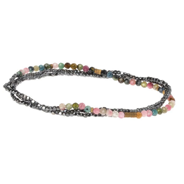 The Scout Jewelry Tourmaline Hematite Delicate Wrap necklace features a mix of small, colorful semi-precious gemstone beads in pink, green, and blue hues, interspersed with metallic black beads. This elegant piece appears as two tightly interwoven strands forming a graceful loop.