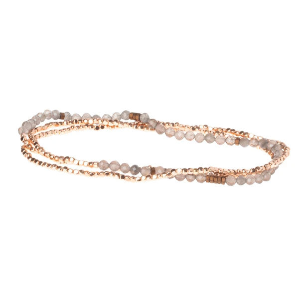 The Smoky Quartz/Rose Gold Delicate Wrap by Scout Jewelry is a thin, multi-strand beaded bracelet with small, round gemstone beads in gold and silver shades, offering an elegant and flexible design for multiple loops.