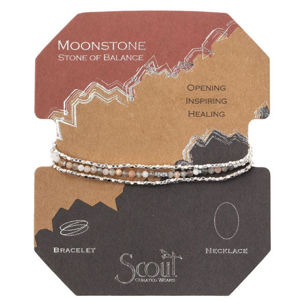 The image depicts a display card for Scout Jewelry, highlighting the Moonstone/Silver Delicate Wrap. This versatile jewelry piece can be worn either as a bracelet or a necklace and features semi-precious moonstone beads and plated brass accents on an elastic cord. The card showcases earthy tones and describes moonstone as the "Stone of Balance," emphasizing its attributes of "Opening, Inspiring, Healing.