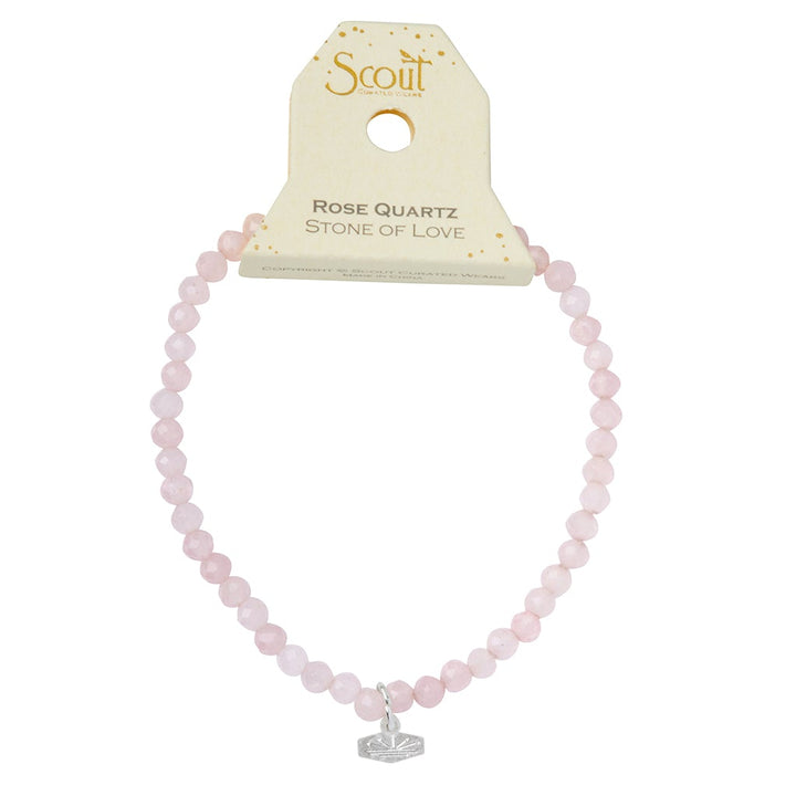 An image of the Mini Bracelet Rose Quartz/Silver, featuring round rose quartz beads and a small silver charm, displayed on a beige cardboard tag labeled "Scout Jewelry." The tag also reads "Rose Quartz Stone of Love," highlighting the bracelet's soft pink color and stretch cord.