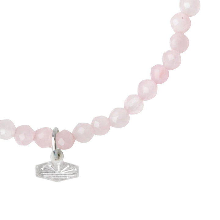 Close-up of a delicate pink bead necklace, the Mini Bracelet Rose Quartz/Silver by Scout Jewelry, featuring round, faceted stone beads and a small silver geometric pendant hanging from the center. The plain white background highlights the exquisite jewelry details.