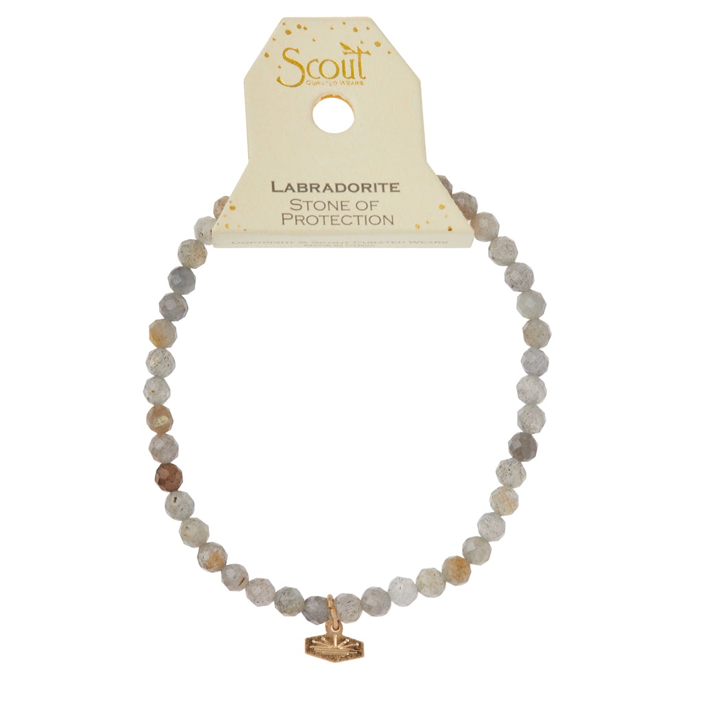 A Mini Bracelet Labradorite/Silver, featuring semi-precious labradorite gemstones with a delicate charm attached, is displayed against a white background. The packaging at the top bears the brand name "Scout Jewelry" and the description "Labradorite Stone of Protection." This elegant bracelet is strung on a durable stretch cord.