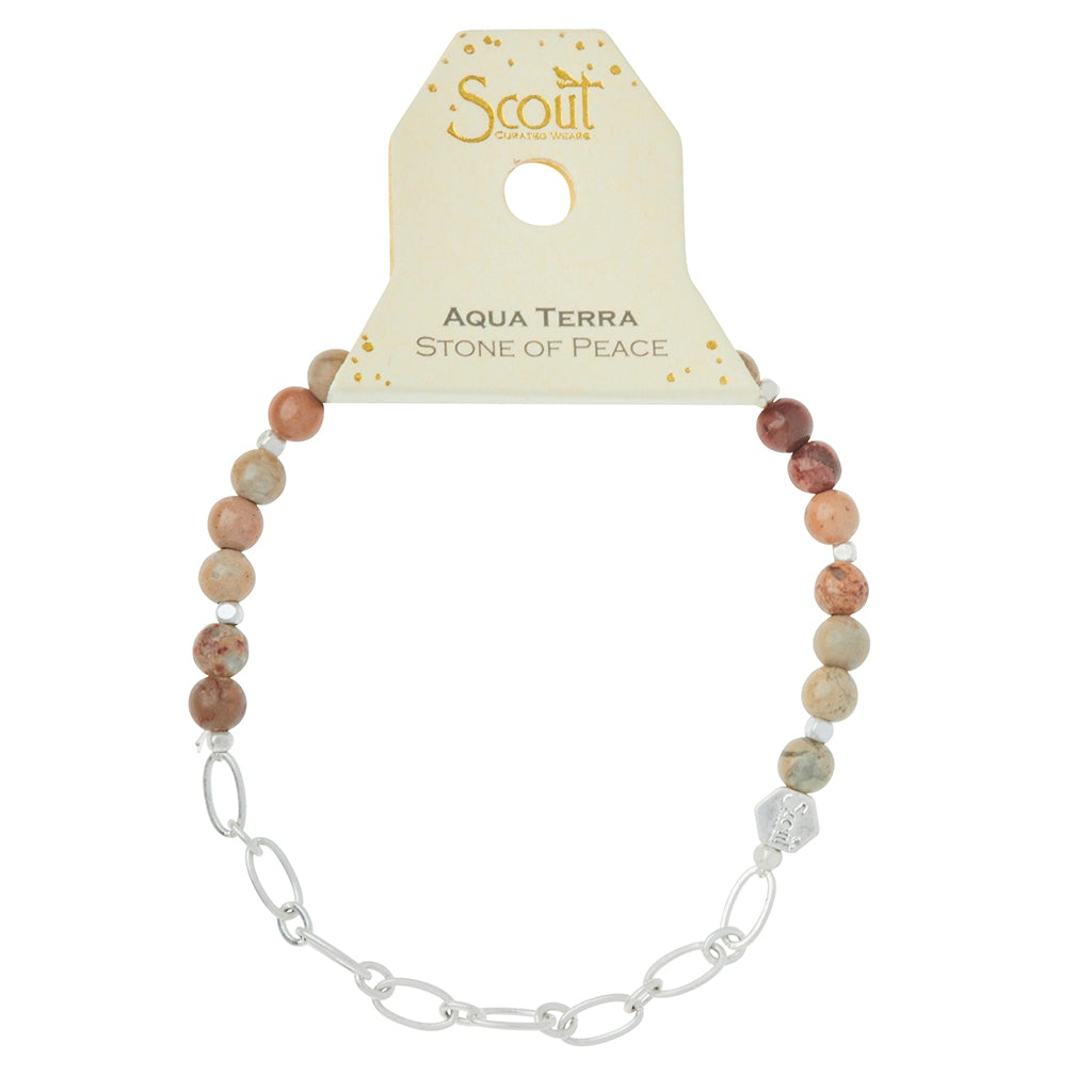 A bracelet named "Chain Bracelet Aqua Terra/Silver" from Scout Jewelry features round aqua terra stones in earthy tones, along with a silver paperclip chain accent and an engraved logo bead for an added touch of elegance. It is labeled as the "Aqua Terra Stone of Peace.