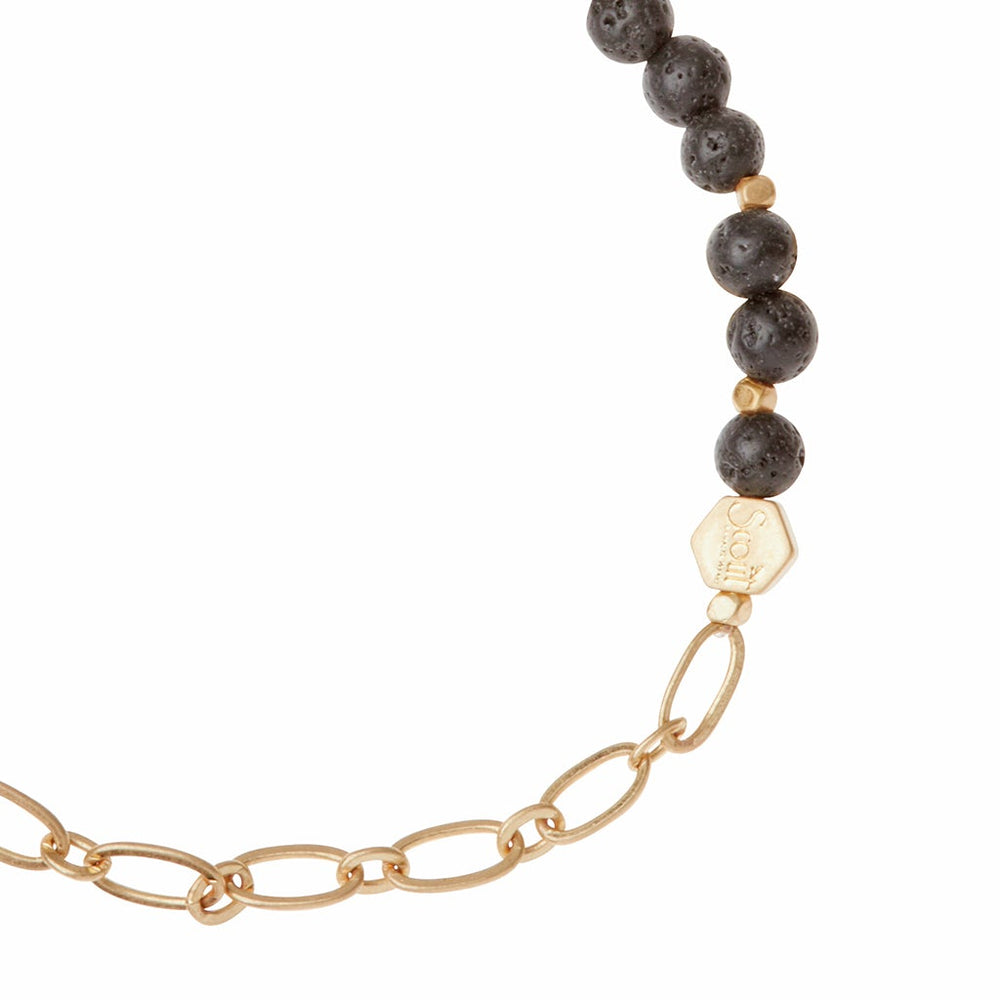 The Chain Bracelet Lava/Gold by Scout Jewelry features black round beads and gold links that blend seamlessly into a paperclip chain on one side, accented with a small gold hexagonal charm near the bead-chain connection. This elegant and modern piece captures attention with its stylish design.