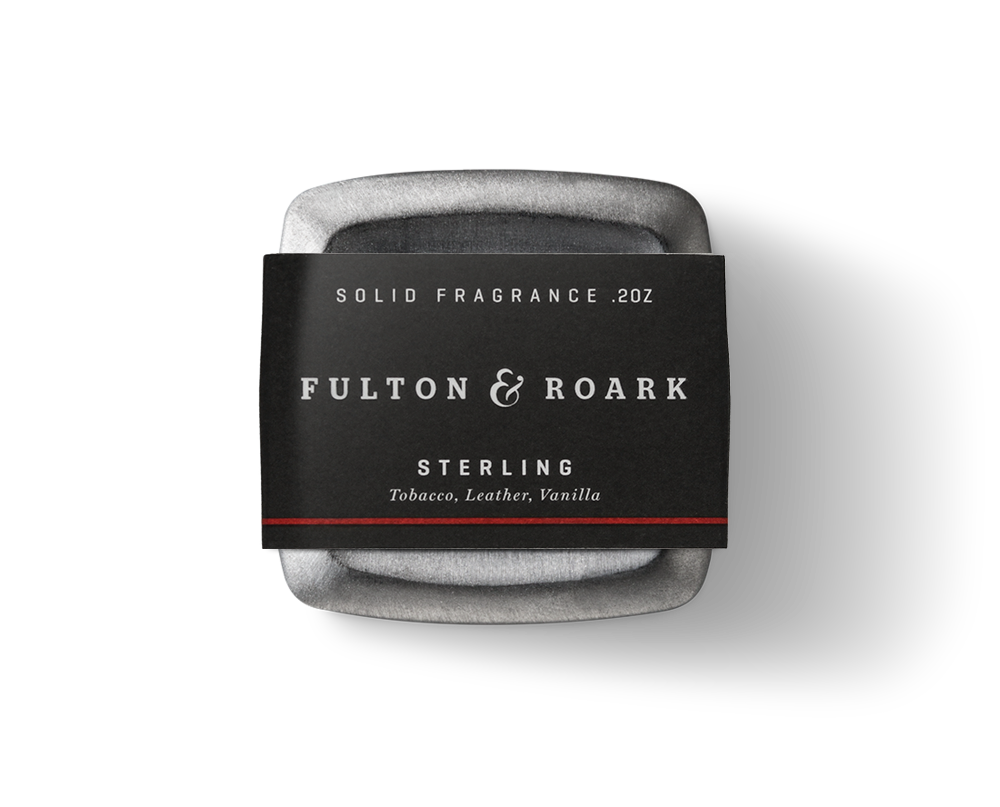 A solid fragrance named "Sterling .2oz" is housed in a square, gray metallic container from the brand Fulton & Roark, featuring rich scents of tobacco and leather with a hint of vanilla.