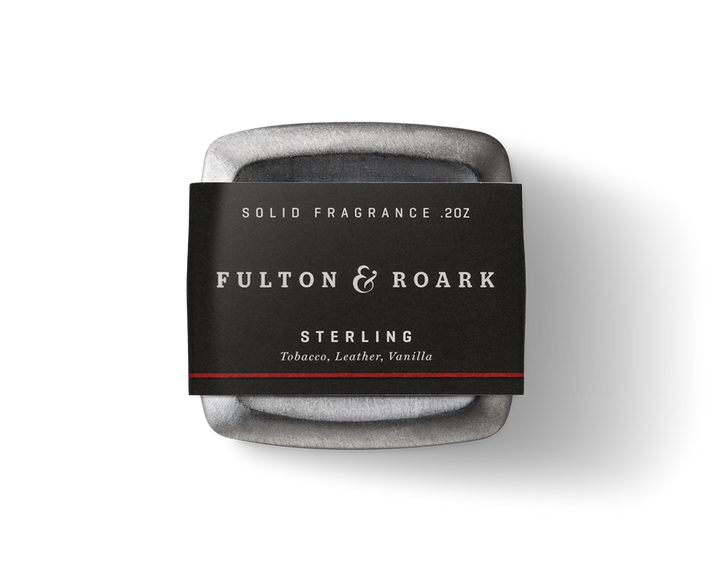 A solid fragrance named "Sterling .2oz" is housed in a square, gray metallic container from the brand Fulton & Roark, featuring rich scents of tobacco and leather with a hint of vanilla.