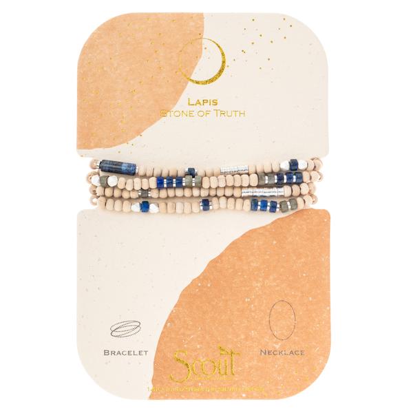 The Lapis/Silver Stone of Truth set by Scout Jewelry includes a beaded bracelet and necklace on a card crafted from renewable wood. It features mainly white beads with blue and dark gray accents from semi-precious stones. The card reads "Lapis, Stone of Truth" with illustrations for both pieces.