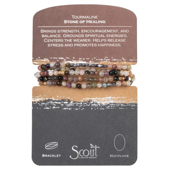 A card showcases multicolored beaded jewelry labeled as "Stone Wrap Tourmaline Hematite/Gold," highlighting the benefits of strength, balance, and stress relief. The semi-precious gemstones are strung on a versatile stretch cord, allowing it to be worn as a bracelet or necklace. The brand "Scout Jewelry" is visible at the bottom.