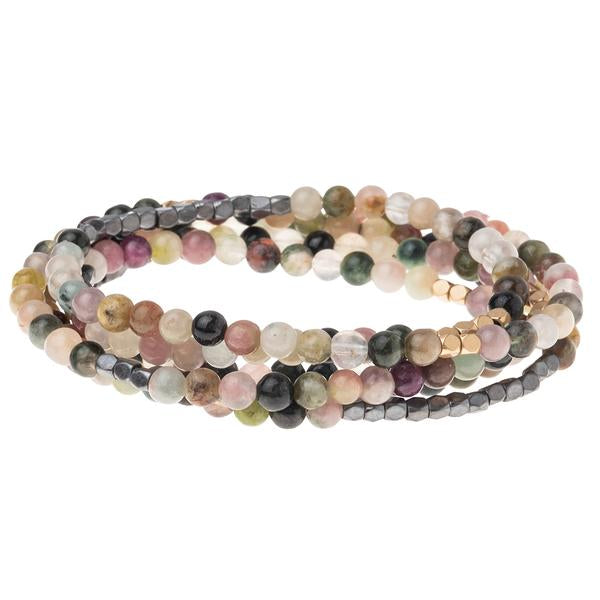 The Stone Wrap Tourmaline Hematite/Gold by Scout Jewelry is a vibrant beaded bracelet showcasing semi-precious gemstones in an array of pink, green, yellow, and black hues. The elastic stretch cord is coiled into multiple loops, and the polished stones boast a glossy finish.