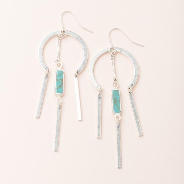 Introducing the Dreamcatcher Earring Turquoise Silver from Scout Jewelry: a stunning pair of 14k gold and silver dangle earrings featuring a circular design. Each earring showcases three vertical bars hanging elegantly from the circle, with a small rectangular turquoise semi-precious stone suspended in the center. These nickel and cadmium-free earrings are completed with a convenient fishhook fastening for easy wear.