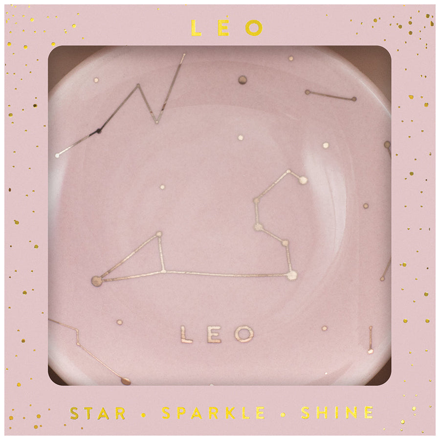 In a square, star-studded pink box, LuckyFeather's Dish Leo features a decorative Zodiac Trinket Dish with the Leo constellation design. The constellation is illustrated with gold dots and lines, while the text "LEO" appears below it on the plate. The box is labeled "LEO" at the top and "STAR SPARKLE SHINE" at the bottom.