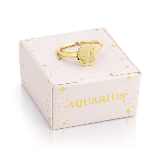 The LuckyFeather Aquarius Signet Ring, dipped in 14k gold and engraved with the Aquarius zodiac symbol, rests on a cream-colored box decorated with golden star patterns and "AQUARIUS" in gold lettering.