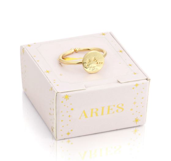 A 14k gold-dipped Aries Signet Ring by LuckyFeather is elegantly displayed on a light-colored box decorated with star patterns and the word "Aries" in gold letters.