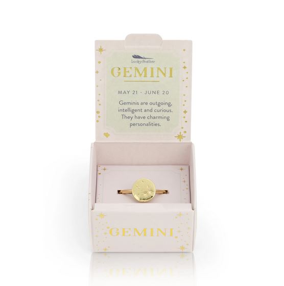 A Gemini Signet Ring from LuckyFeather, featuring a 14k gold-dipped circular design, is displayed in an open box adorned with celestial decorations. This zodiac ring celebrates Gemini traits such as being outgoing, intelligent, and curious, and showcases their birth dates, May 21 - June 20.