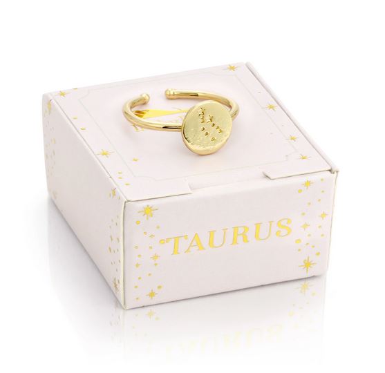 The LuckyFeather Taurus Signet Ring, a 14k gold-dipped piece with a round face engraved with the Taurus constellation, is displayed atop a cream-colored box. The adjustable band ring's packaging features small star decorations and the word "Taurus" in light gold lettering.