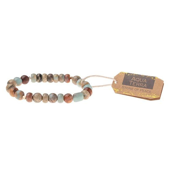 The Aqua Terra Stone Stacking Bracelet by Scout Jewelry features a mix of turquoise, brown, and beige semi-precious gemstone beads. Designed on a stretch cord for comfort, the bracelet is accompanied by a small brown tag with the text "Aqua Terra" and "Stone of Peace.