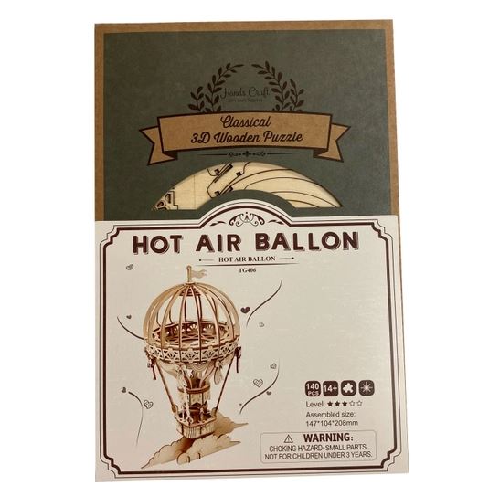 A package in a modern vintage style showcases Hands Craft's classic 3D Wooden Puzzle Hot Air Balloon. The image features the assembled model with 144 pieces, suitable for ages 14 and up. A warning about small parts and choking hazards is prominently displayed.