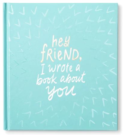 The "Friend wrote a book about you" by Compendium features a turquoise cover adorned with light blue and white diagonal lines. The center showcases the title, "Hey friend, I wrote a book about you," in a casual handwritten font. This friendship keepsake is filled with whimsical prompts designed to capture precious memories and moments.