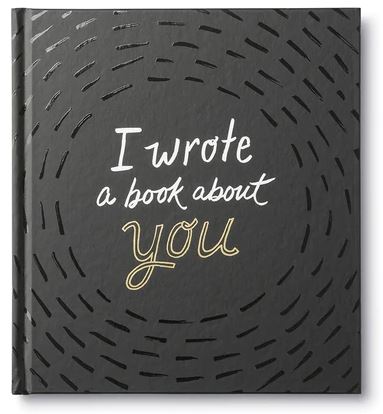 A personalized Compendium book titled "I wrote a book about you" features a black cover adorned with white and gold lettering. The background displays a pattern of short, curved black lines radiating from the center, making it an ideal meaningful gift for any occasion.