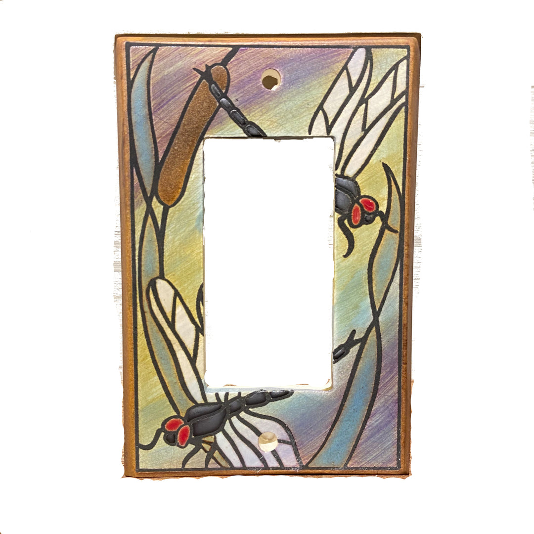 The "Rocker Dragonfly Bulrush" by ALL FIRED UP is a decorative rocker light switch cover inspired by stained glass. It features colorful dragonflies and cattails on a multicolored background, with cutouts for the switch and screws.