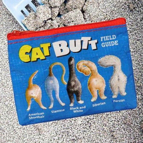 The "Cat Butt Coin Purse" by Blue Q is a colorful pouch adorned with humorous illustrations of cat rear ends from various breeds, including American Shorthair, Siamese, Black and White, Siberian, and Persian. Measuring 3 inches in height by 4 inches in width and made from recycled material, the purse is displayed on a pebble-covered surface.