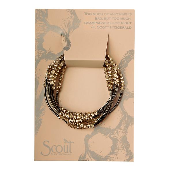 A beaded necklace set on a beige card elegantly captures Fitzgerald's wit: "Too much of anything is bad, but too much champagne is just right." The brand, Scout Jewelry, is subtly showcased at the bottom, hinting at the sophisticated charm of the Wrap champagne/hematite - Too Much of Anything collection.