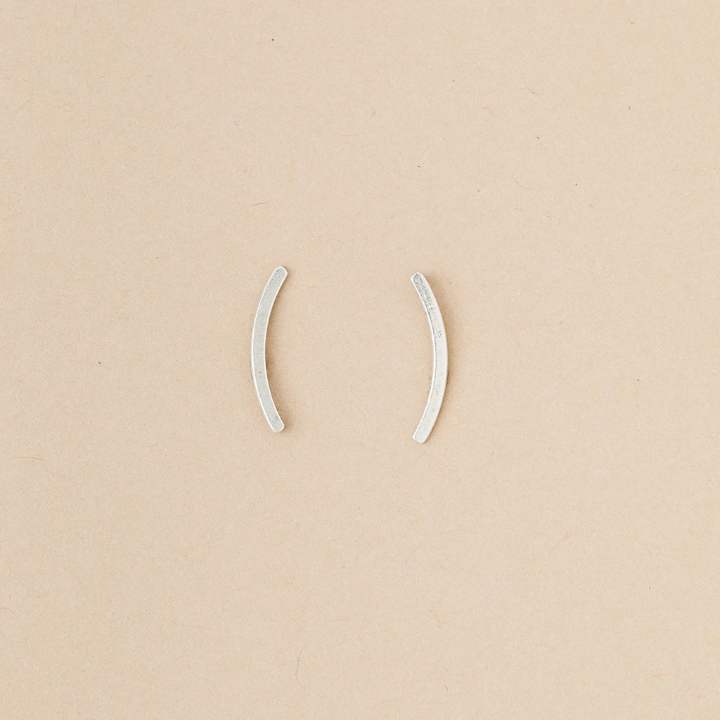 Part of Scout Jewelry's Comet Curve Silver collection, these two small, curved ear cuffs are elegantly displayed on a beige background.