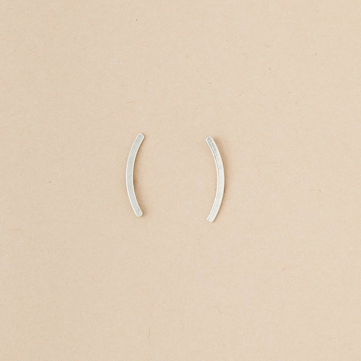 Part of Scout Jewelry's Comet Curve Silver collection, these two small, curved ear cuffs are elegantly displayed on a beige background.