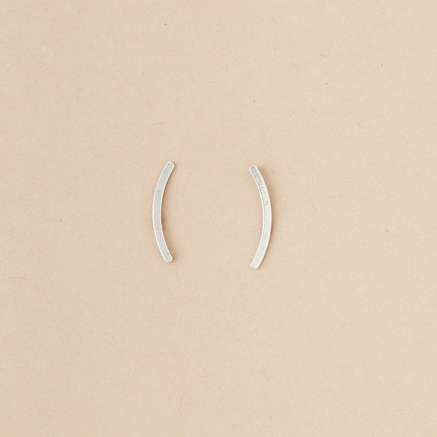 Part of Scout Jewelry's Comet Curve Silver collection, these two small, curved ear cuffs are elegantly displayed on a beige background.