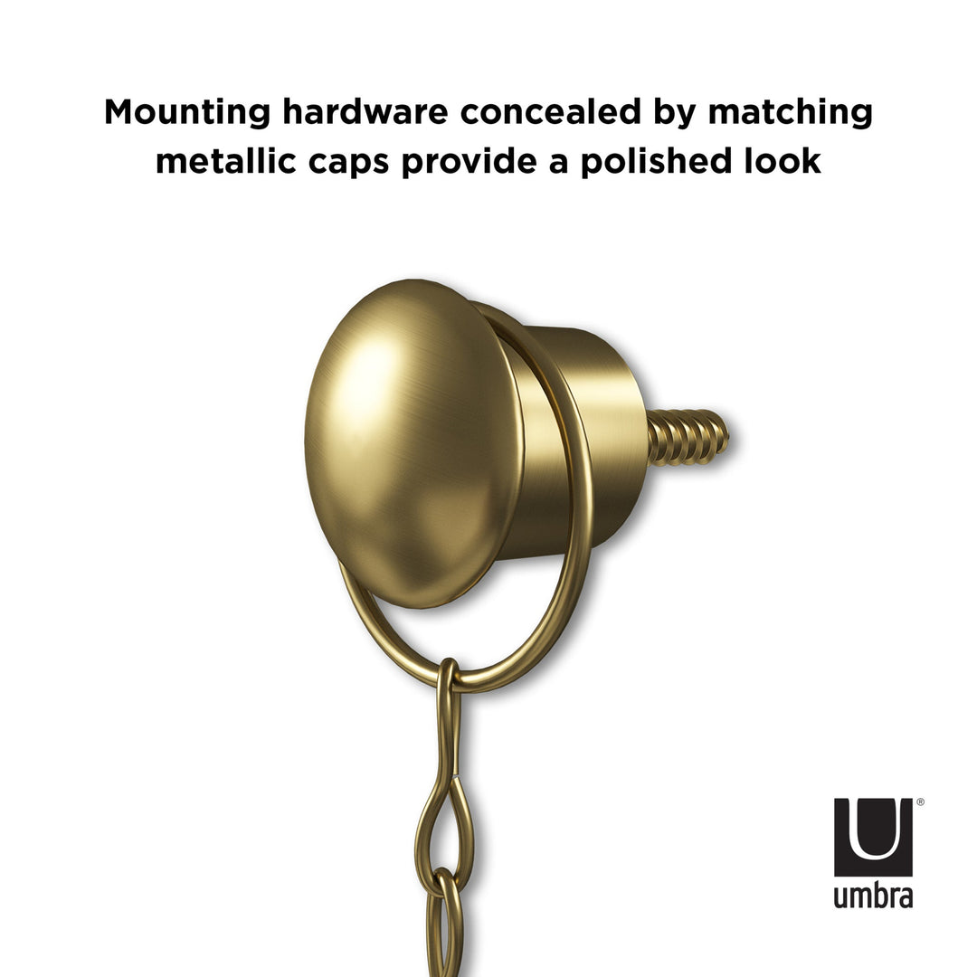 A gold-toned screw with a matching metallic cap attaches to a chain, crafting the elegant Diamond Mirror Brass decor piece. Text states: "Mounting hardware concealed by matching metallic caps provides a polished look." Umbra logo is positioned in the bottom right corner.