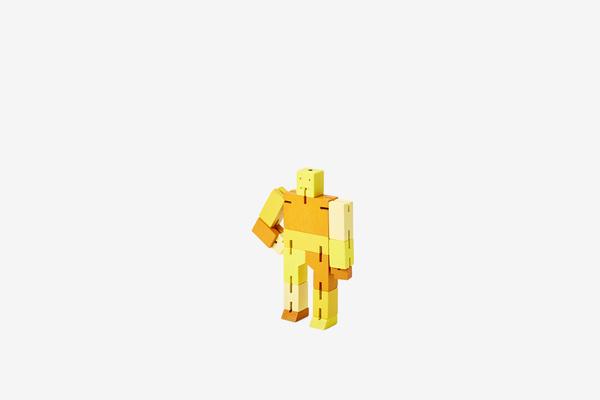 The Cubebot Micro Yellow Multi from Areaware is a small, blocky humanoid figure in yellow and orange, set against a plain white background. Reminiscent of wooden toy robots, it features articulated joints that enable a variety of poses.