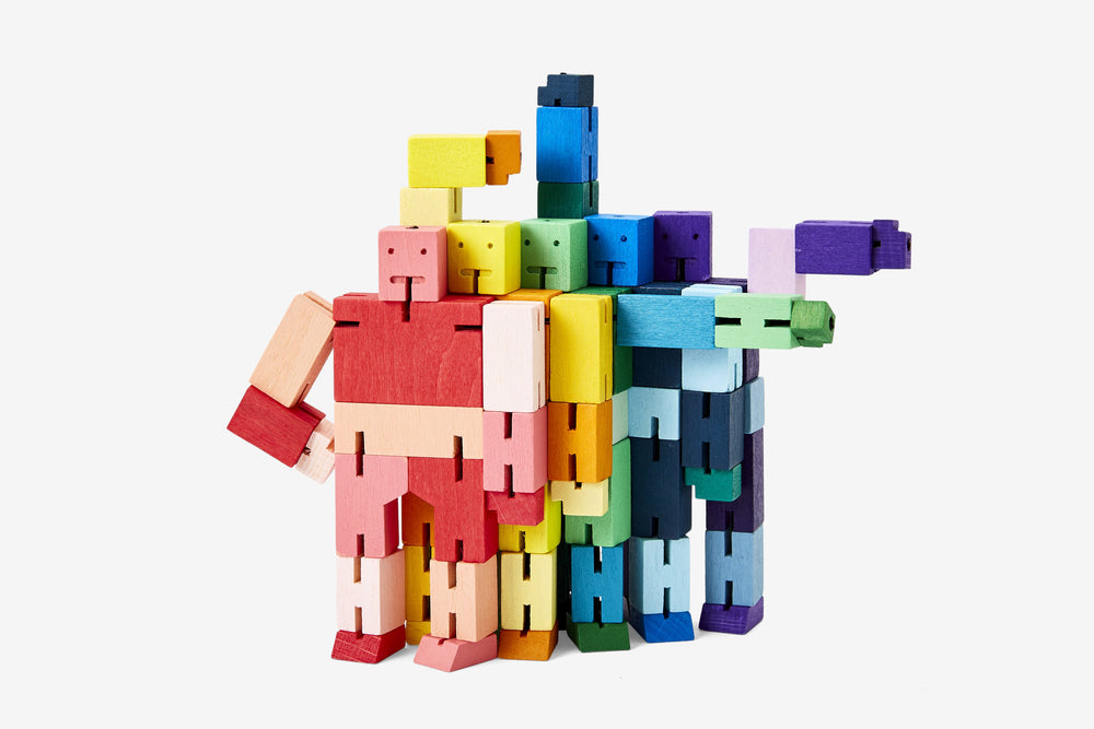 The Cubebot Micro Yellow Multi figures from Areaware, featuring an array of colors such as red, yellow, green, blue, and purple, are arranged in a playful formation. The figures mimic the poseability of Cubebot Mini Red with their arms bent or extended to create a vibrant geometric pattern reminiscent of Shinto Kumi-ki puzzles against a white backdrop.