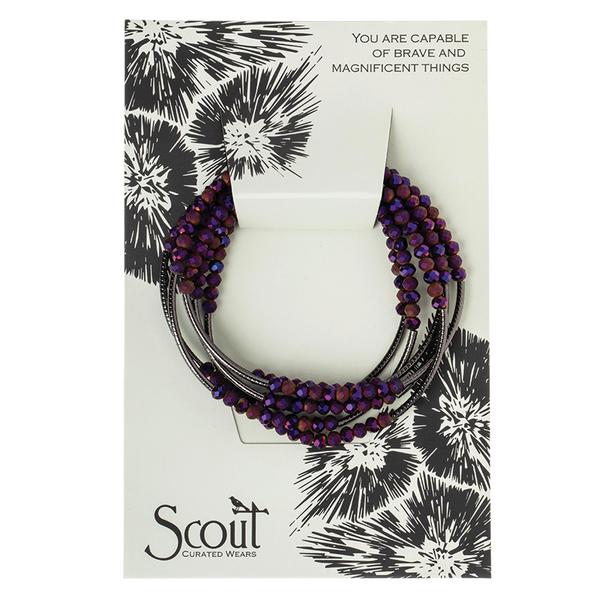 A Wrap Dahlia Hematite bracelet featuring purple and black beads is displayed on a card decorated with floral designs and the phrase "You are capible of brave and magnificent things." The brand name "Scout Jewelry" is elegantly printed at the bottom, adding a touch of charm.