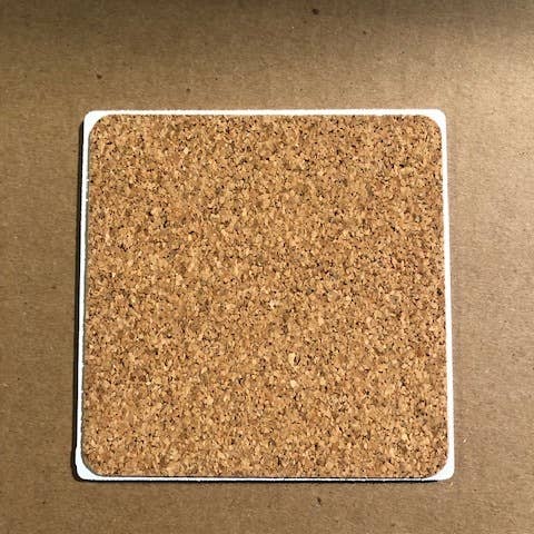 A square cork coaster with rounded edges on a brown background, named the Internet Stopped coaster by Drinks On Me. This minimalist piece features a natural cork texture and remains simple and unadorned.