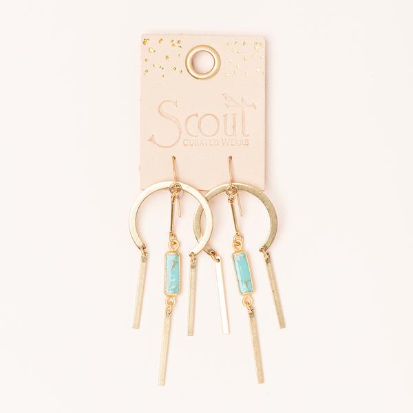 A pair of Dreamcatcher Earring Turquoise Gold is displayed on a beige card with the brand name "Scout Jewelry" at the top. These 14k gold earrings feature circular hoops with rectangular turquoise semi-precious stones and dangling gold bars, ensuring they are nickel and cadmium free.