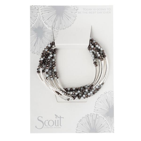 A set of multi-strand Wrap Eclipse/Silver bracelets adorned with dark and light beads comes on a card. This card, decorated with a floral design and the inspirational message "today is going to be the best," embodies the essence of an eclipse. The brand name "Scout Jewelry" is beautifully displayed at the bottom left.