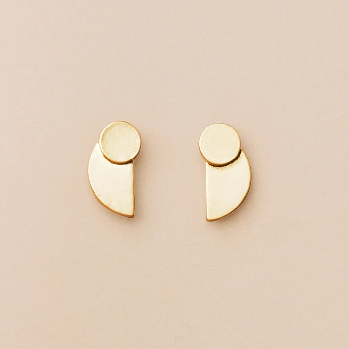 From the Refined Earring Collection, the Eclipse Stud Gold earrings by Scout Jewelry are crafted in 18k gold vermeil and showcased against a light beige background. These minimalist pieces feature small circular and semi-circular shapes arranged in a modern, geometric design.