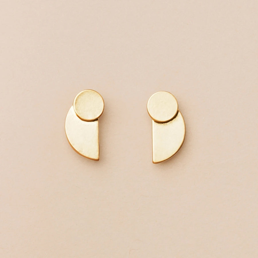 From the Refined Earring Collection, the Eclipse Stud Gold earrings by Scout Jewelry are crafted in 18k gold vermeil and showcased against a light beige background. These minimalist pieces feature small circular and semi-circular shapes arranged in a modern, geometric design.