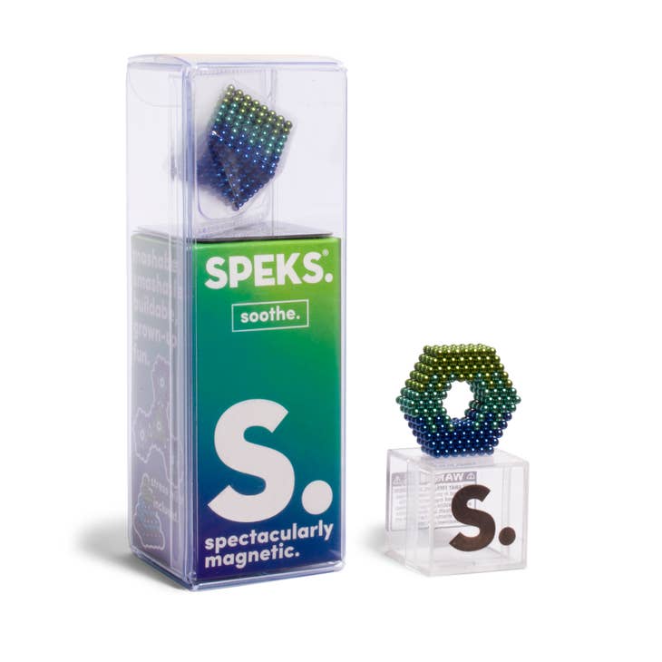 A package of "512 Soothe Speks" magnetic beads arranged in various shapes. The clear plastic box has a gradient green and blue label with the text "spectacularly magnetic" and showcases a hexagonal ring of rare earth magnet beads on top. An additional bead figure is displayed beside this fidget toy.