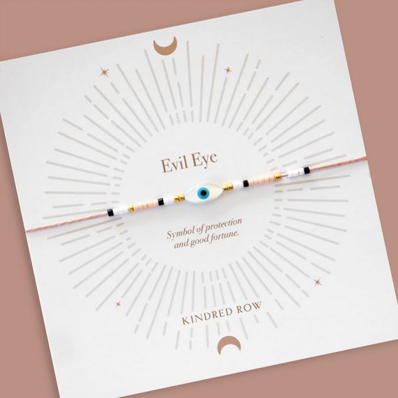 The Evil Eye Cord Bracelet Dusty Rose by Kindred Row features an evil eye design with black, white, and mother of pearl beads. It is presented on a card that reads "Evil Eye: Symbol of protection and good fortune," embellished with decorative lines and crescent moons.