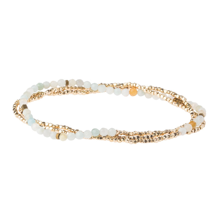 The Amazonite Gold Delicate Wrap by Scout Jewelry is a refined bracelet featuring gold-toned beads mixed with small, round, light-colored semi-precious amazonite gemstones. The bracelet is displayed coiled in a loop.