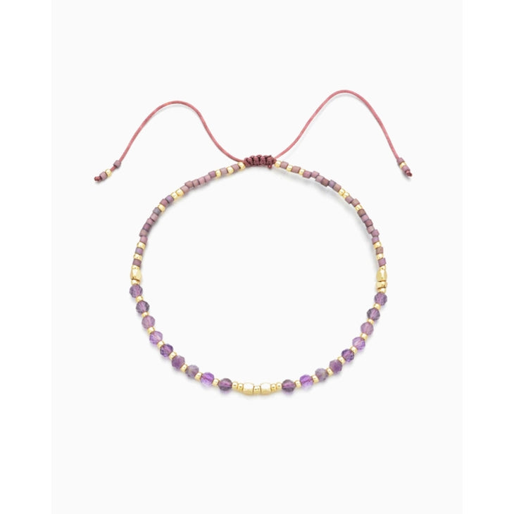 Introducing the Kindred Row Amethyst Healing Gemstone Stacking Bracelet, a delicate handmade piece adorned with natural amethyst gemstones and vibrant purple and gold beads, all elegantly strung on a fine pink cord with an adjustable closure for the perfect fit.