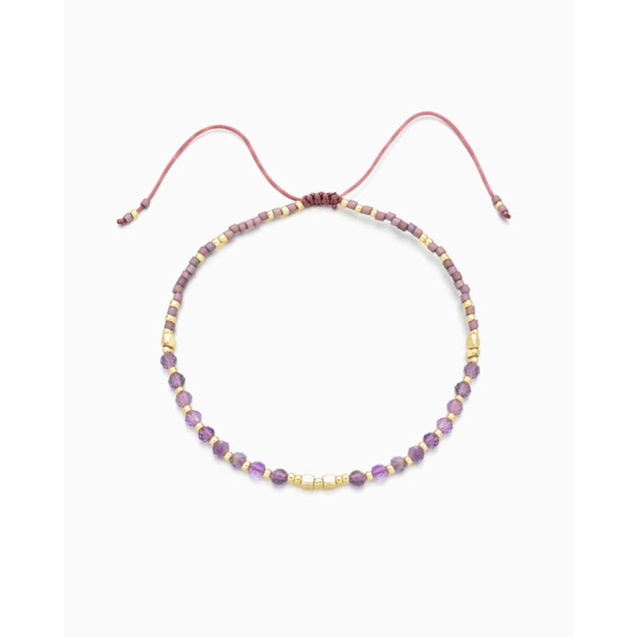 Introducing the Kindred Row Amethyst Healing Gemstone Stacking Bracelet, a delicate handmade piece adorned with natural amethyst gemstones and vibrant purple and gold beads, all elegantly strung on a fine pink cord with an adjustable closure for the perfect fit.